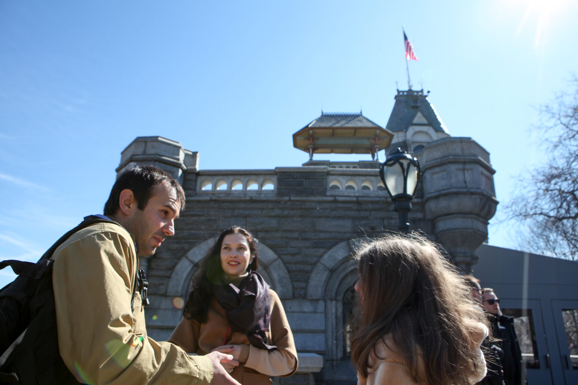 a guide whose facial expression is one of disgusted disbelief is looking at one of his younger guests while her mom poses in front of the Belvedere Castle in Central Park
