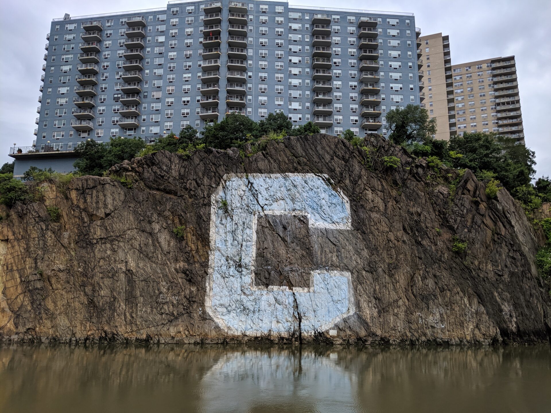 Large blue C letter on a side of a cliff over muddy water