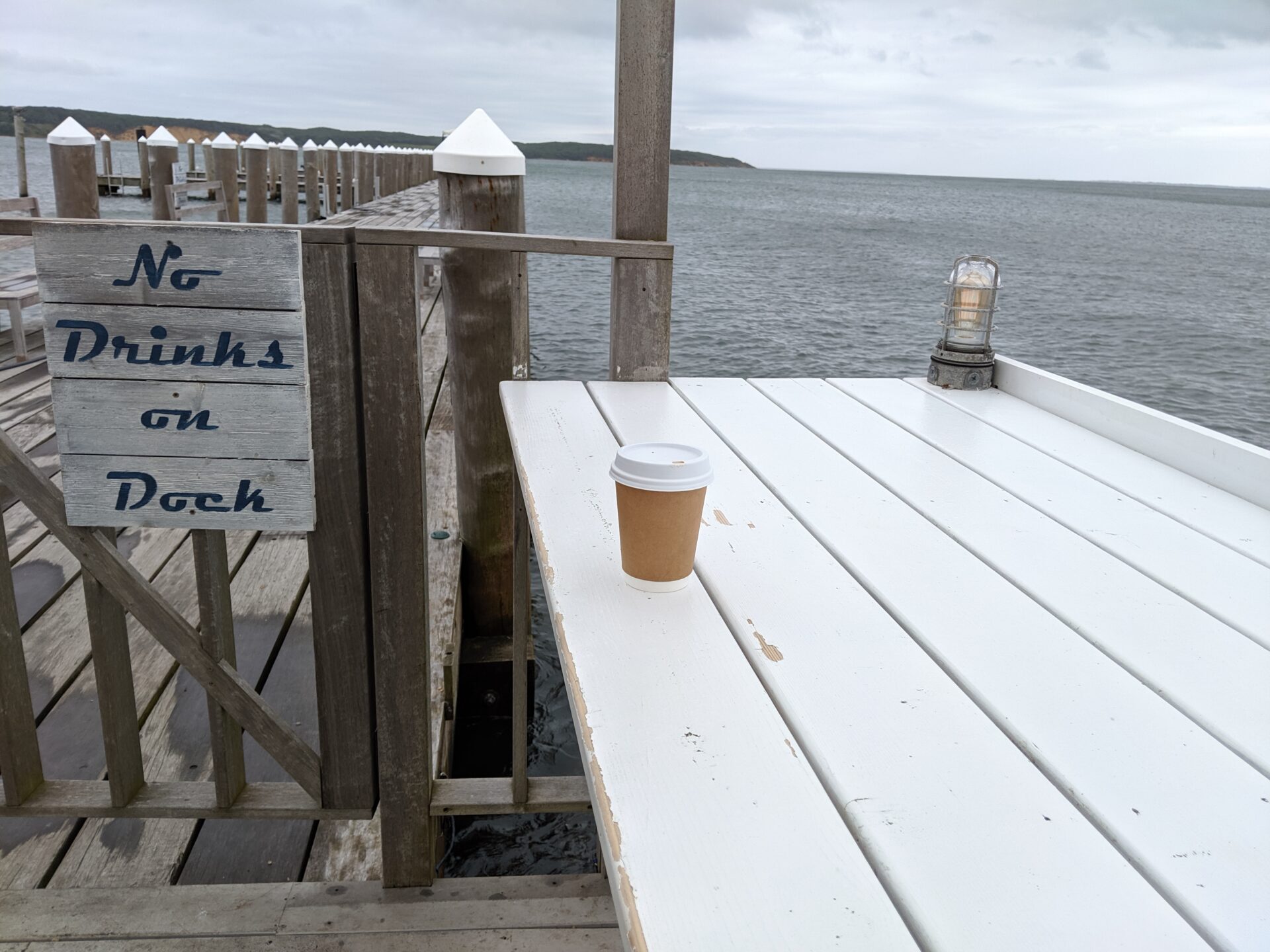 a coffee cup on an outdoor table with a view of the water near a dock